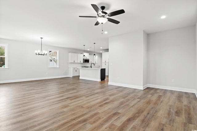 unfurnished living room featuring sink, ceiling fan with notable chandelier, and light wood-type flooring