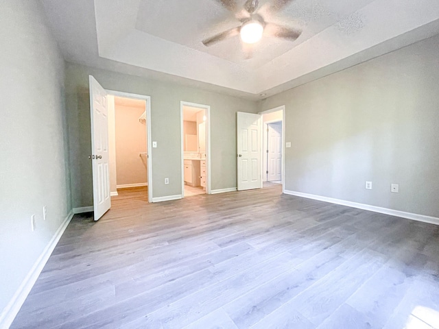 unfurnished bedroom with a tray ceiling, a spacious closet, ensuite bath, and hardwood / wood-style flooring