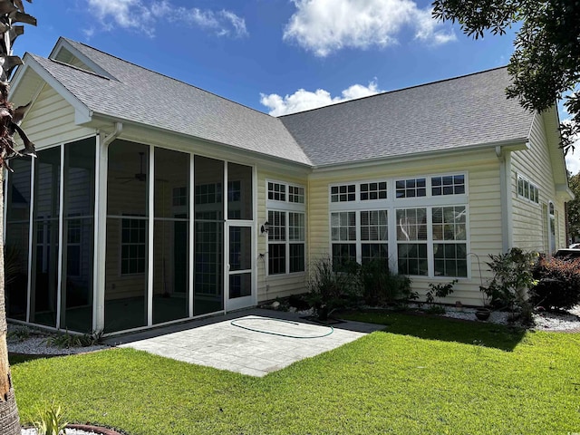 back of property featuring a sunroom, a patio area, roof with shingles, and a lawn