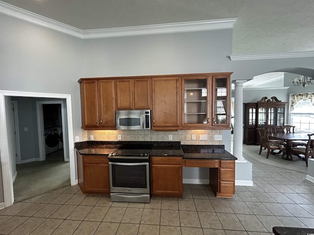 kitchen with brown cabinets, stainless steel appliances, dark countertops, light tile patterned flooring, and washer / dryer