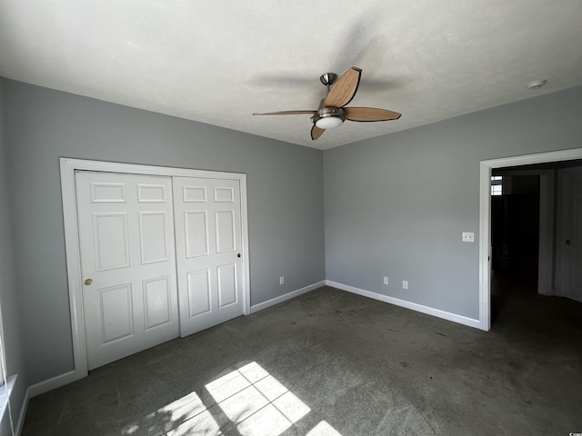 unfurnished bedroom featuring baseboards, a ceiling fan, a textured ceiling, dark carpet, and a closet