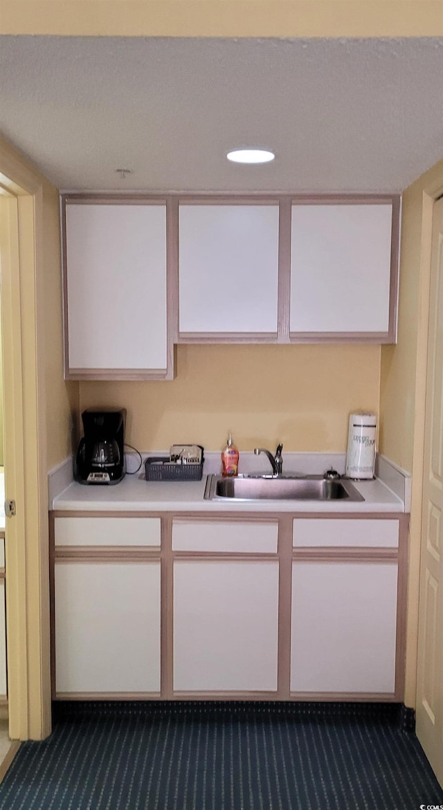 kitchen featuring white cabinets, sink, dark colored carpet, and a textured ceiling