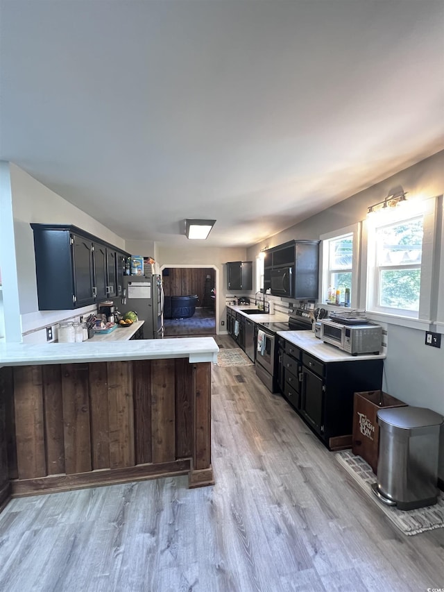 kitchen featuring stainless steel appliances, sink, light wood-type flooring, and kitchen peninsula