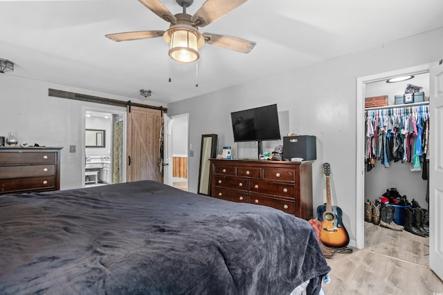 bedroom with a spacious closet, light hardwood / wood-style flooring, a closet, ceiling fan, and a barn door