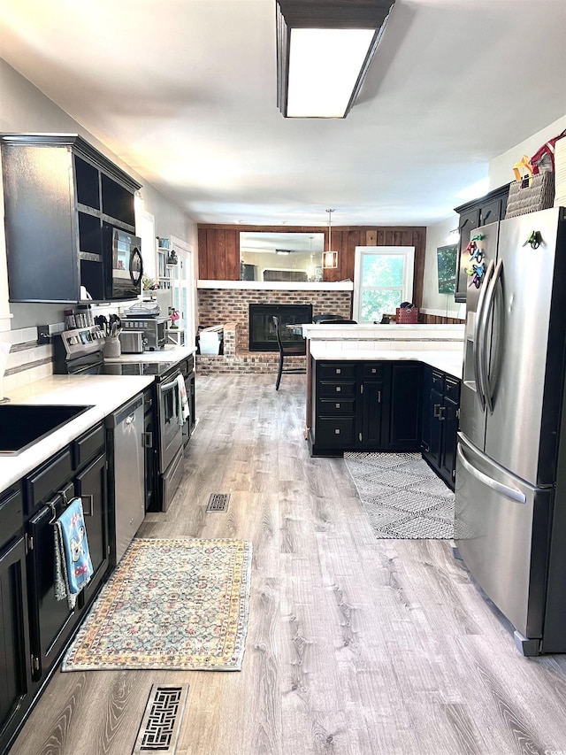 kitchen with sink, kitchen peninsula, pendant lighting, stainless steel appliances, and light hardwood / wood-style floors