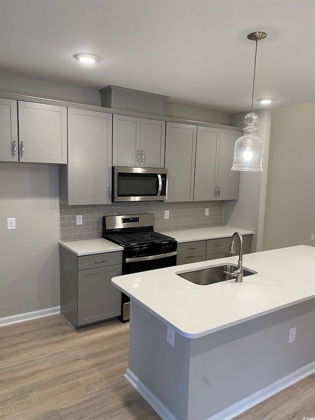 kitchen featuring stainless steel appliances, sink, light wood-type flooring, gray cabinetry, and pendant lighting