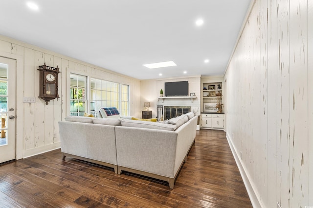 living room featuring dark hardwood / wood-style flooring, a skylight, built in shelves, crown molding, and wooden walls