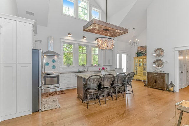 kitchen with light wood-type flooring, high vaulted ceiling, ventilation hood, range, and white cabinets