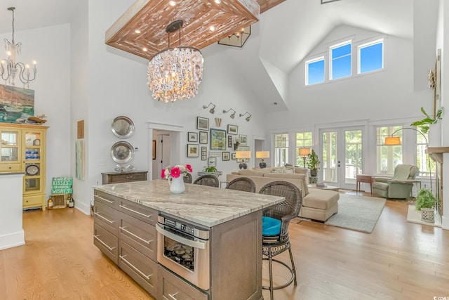 kitchen featuring a towering ceiling, stainless steel oven, an inviting chandelier, and light hardwood / wood-style floors