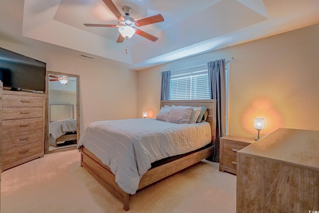 carpeted bedroom with a raised ceiling and ceiling fan