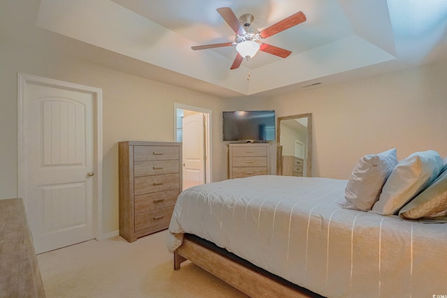 bedroom featuring light colored carpet, ceiling fan, a tray ceiling, and connected bathroom