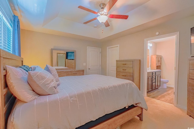 bedroom featuring ensuite bathroom, ceiling fan, a tray ceiling, and light carpet