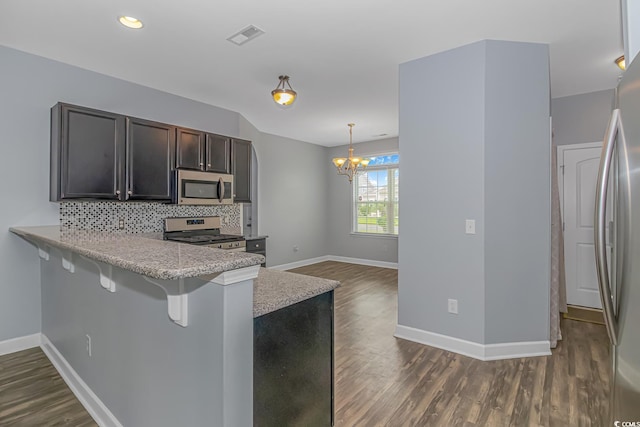 kitchen with kitchen peninsula, decorative light fixtures, tasteful backsplash, appliances with stainless steel finishes, and a breakfast bar area