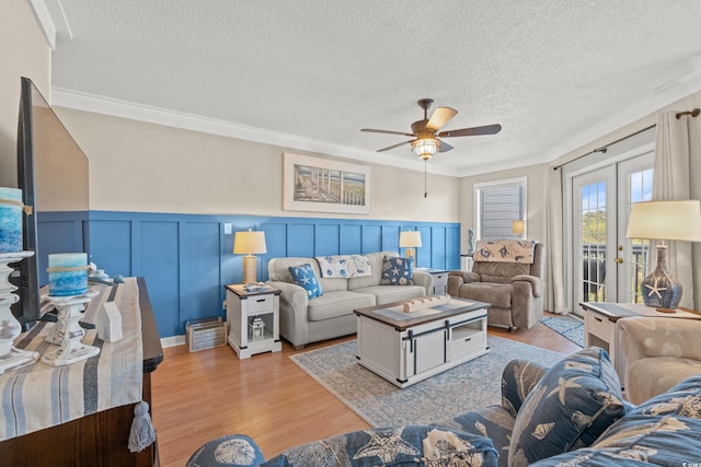 living area with a ceiling fan, light wood-type flooring, french doors, and a textured ceiling