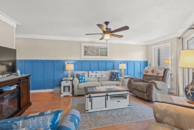 living area featuring ceiling fan, a textured ceiling, ornamental molding, and wood finished floors