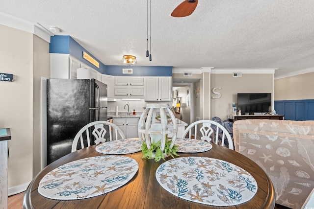 dining space with crown molding, visible vents, a textured ceiling, and wainscoting