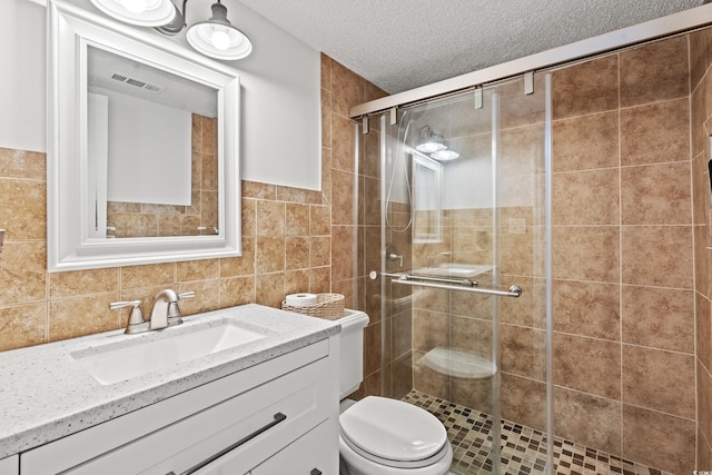 bathroom featuring tile walls, visible vents, toilet, a stall shower, and a textured ceiling