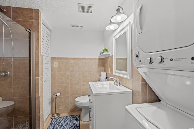 full bathroom featuring tile walls, a shower stall, visible vents, and stacked washer / dryer