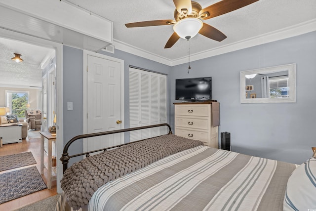 bedroom featuring a ceiling fan, ornamental molding, a textured ceiling, light wood-type flooring, and a closet