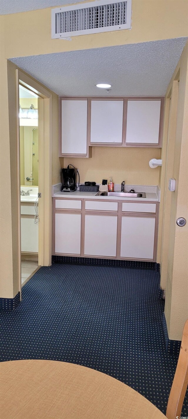 2701 S Ocean Blvd Unit 1410, North Myrtle Beach, SC 29582 - kitchen featuring white cabinetry, dark carpet, light countertops, a sink, and a textured ceiling
