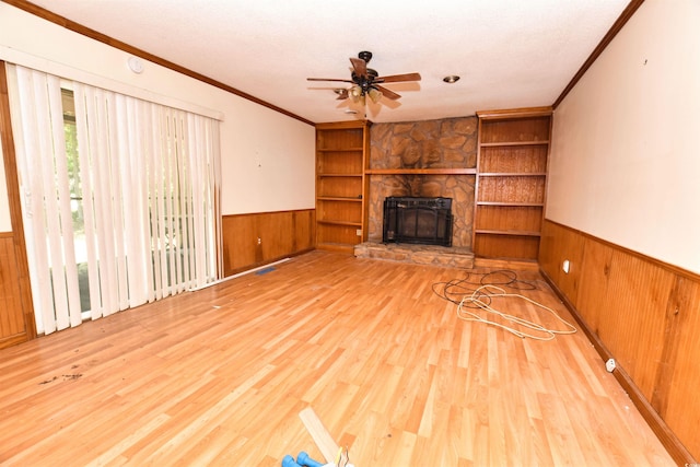 unfurnished living room featuring built in shelves, ceiling fan, a textured ceiling, a fireplace, and light hardwood / wood-style floors