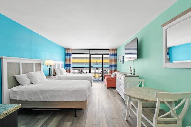 bedroom with access to outside, expansive windows, and wood finished floors