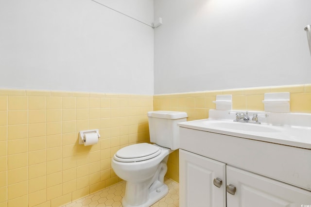 half bath with wainscoting, toilet, tile patterned flooring, vanity, and tile walls