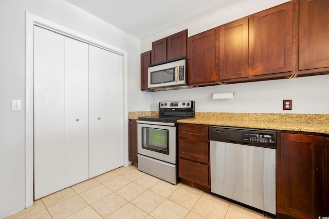 kitchen with a textured ceiling, appliances with stainless steel finishes, light tile patterned flooring, and light stone counters