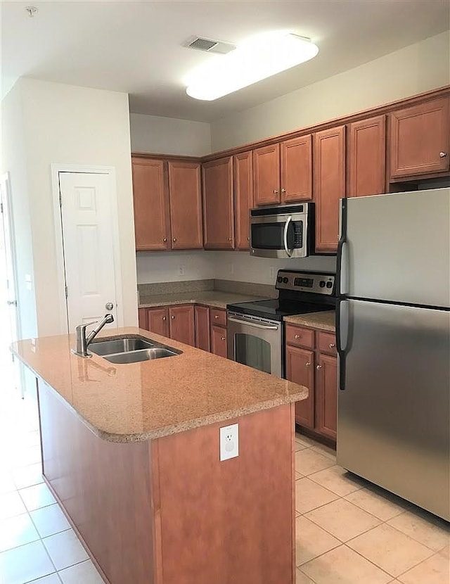 kitchen with sink, appliances with stainless steel finishes, light tile patterned floors, and an island with sink