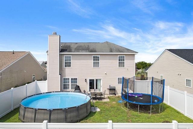 rear view of house with a patio area, a yard, and a trampoline