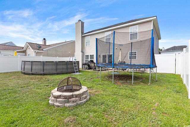 back of house featuring a fire pit, a trampoline, and a lawn