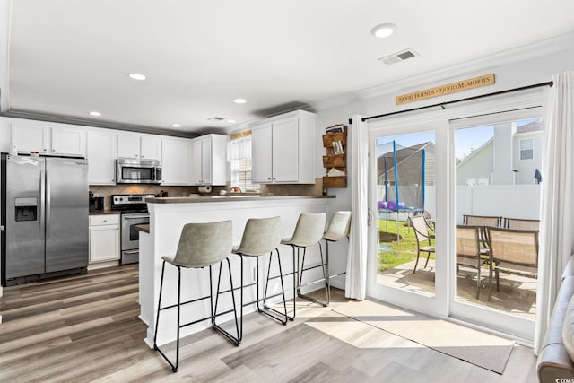 kitchen featuring a breakfast bar, appliances with stainless steel finishes, white cabinetry, and crown molding