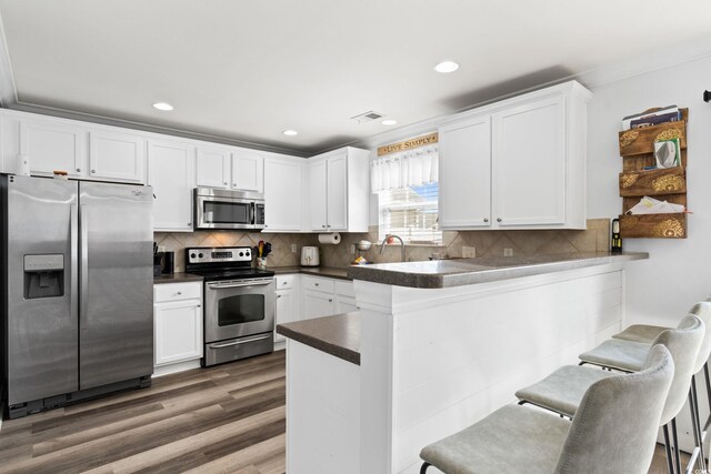 kitchen with a kitchen breakfast bar, kitchen peninsula, white cabinets, and appliances with stainless steel finishes