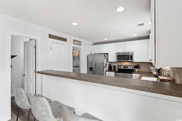 kitchen with kitchen peninsula, decorative backsplash, ornamental molding, appliances with stainless steel finishes, and white cabinetry