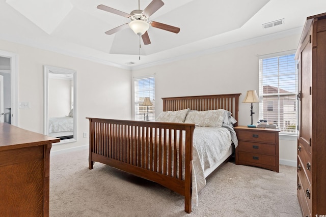 bedroom with multiple windows, light carpet, a tray ceiling, and ceiling fan