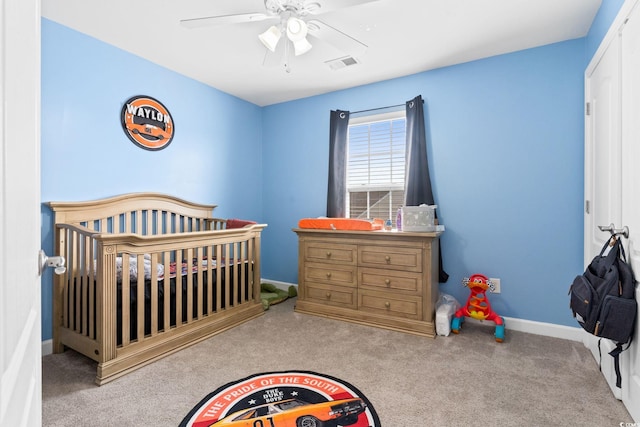 bedroom with a crib, light colored carpet, and ceiling fan