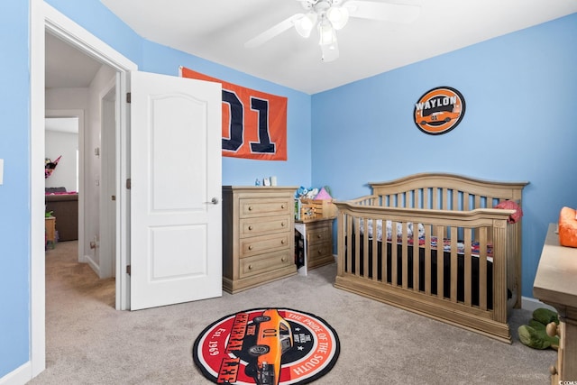 bedroom with light colored carpet, a nursery area, and ceiling fan