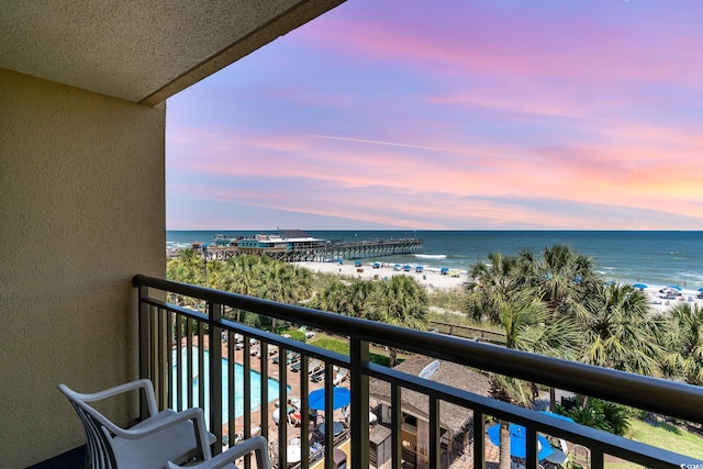 balcony at dusk featuring a water view and a beach view