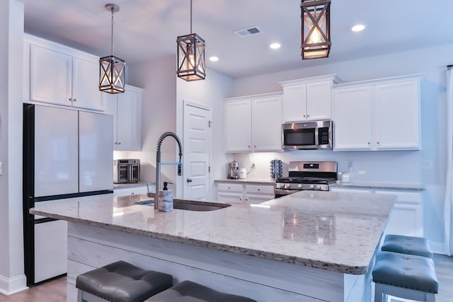 kitchen with hanging light fixtures, appliances with stainless steel finishes, a kitchen bar, and a kitchen island with sink