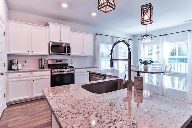 kitchen with decorative light fixtures, hardwood / wood-style flooring, decorative backsplash, light stone counters, and appliances with stainless steel finishes