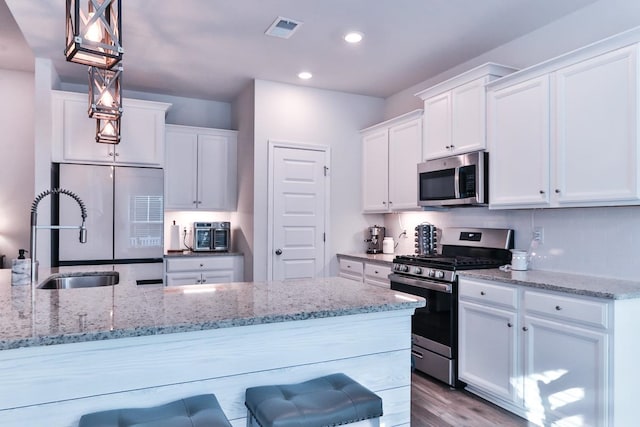 kitchen with white cabinetry, hardwood / wood-style flooring, decorative light fixtures, and appliances with stainless steel finishes