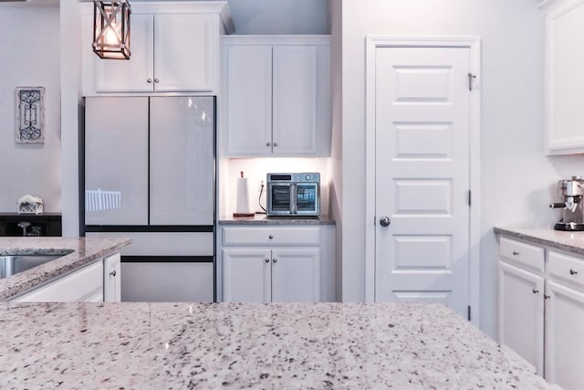 kitchen featuring pendant lighting, light stone counters, white refrigerator, and white cabinetry