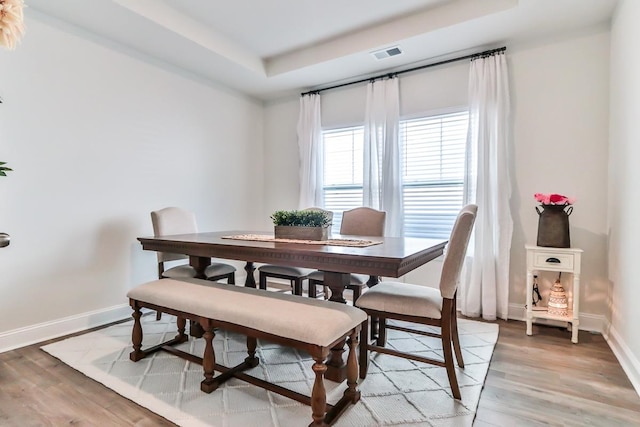 dining room with light wood-type flooring and a tray ceiling