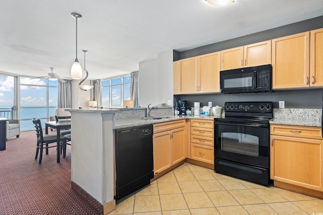 kitchen featuring decorative light fixtures, sink, black appliances, a water view, and light stone countertops