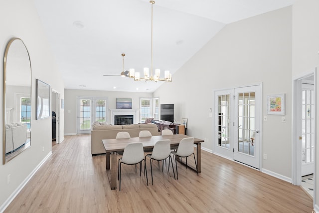 dining area with a chandelier, high vaulted ceiling, baseboards, light wood finished floors, and a glass covered fireplace