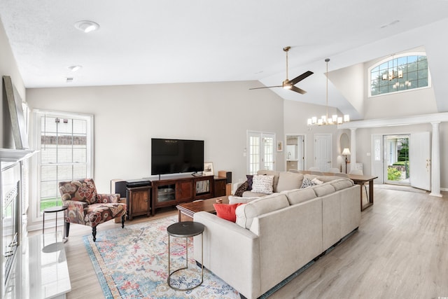 living room with light wood-type flooring, ceiling fan with notable chandelier, and high vaulted ceiling