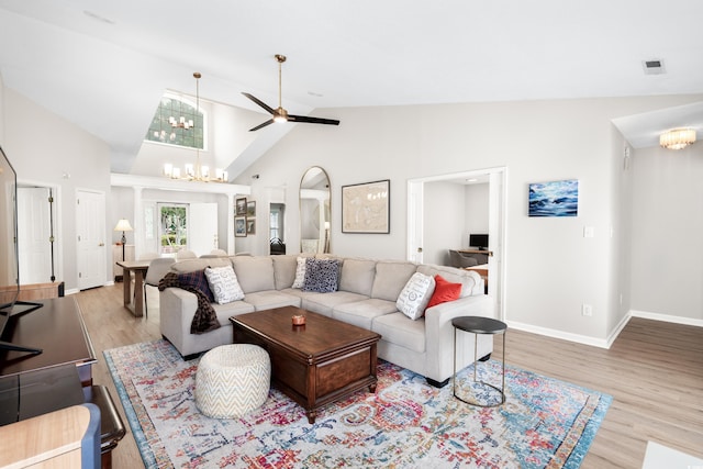 living room featuring high vaulted ceiling, ceiling fan with notable chandelier, wood finished floors, visible vents, and baseboards