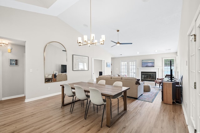 dining area featuring high vaulted ceiling, light hardwood / wood-style floors, and ceiling fan with notable chandelier