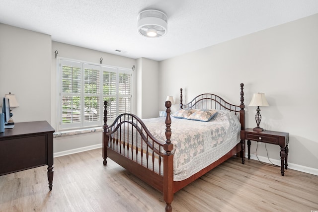 bedroom with light wood-style flooring, visible vents, baseboards, and a textured ceiling