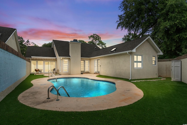 pool at dusk with a patio and a lawn